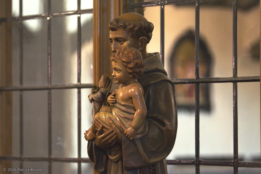 A carved statue of St. Anthony holding the Christ Child beside a leaded window